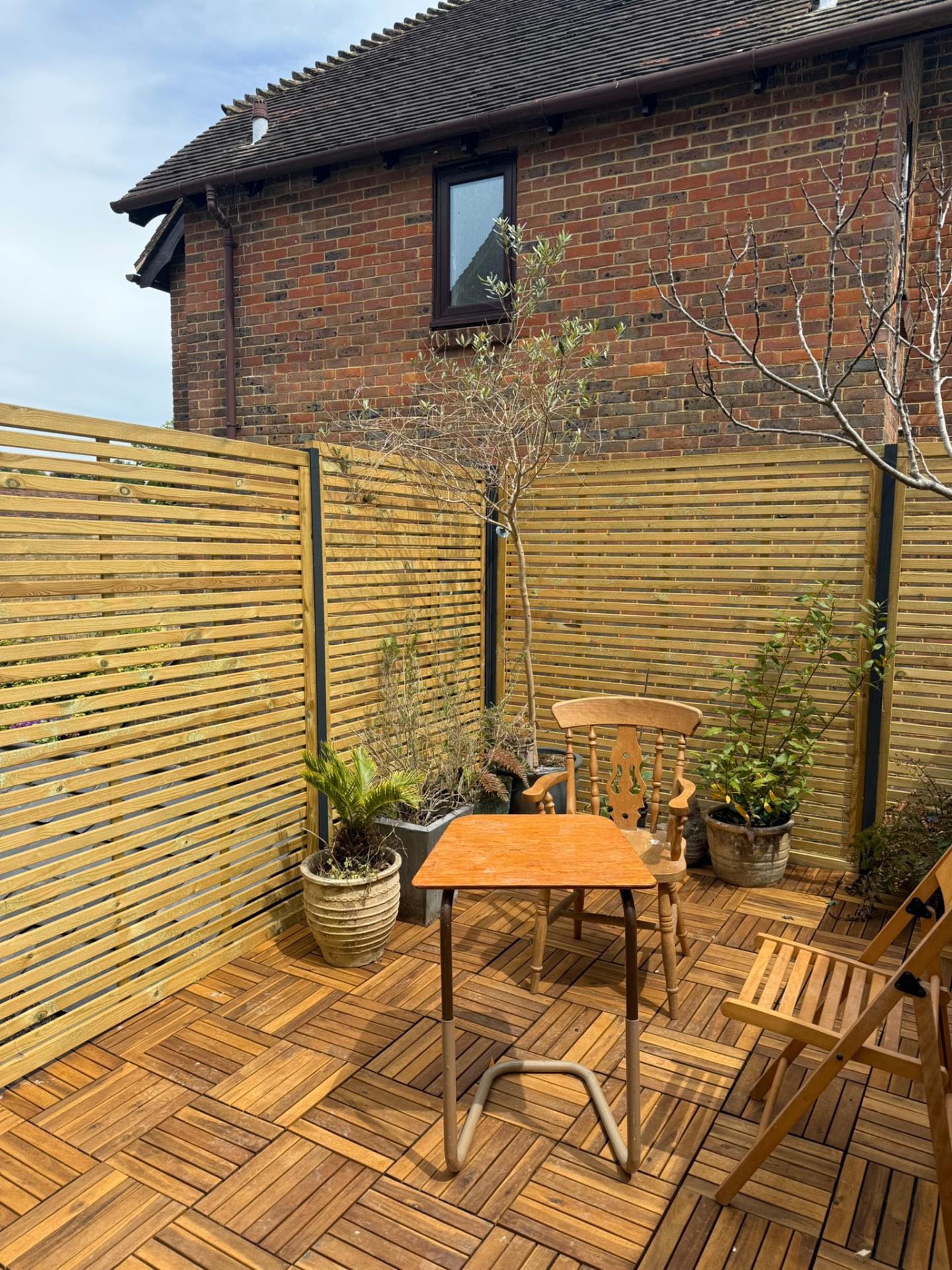 Roof garden with horizontal slatted timber screens on steel posts surrounding a herringbone-pattern wooden deck