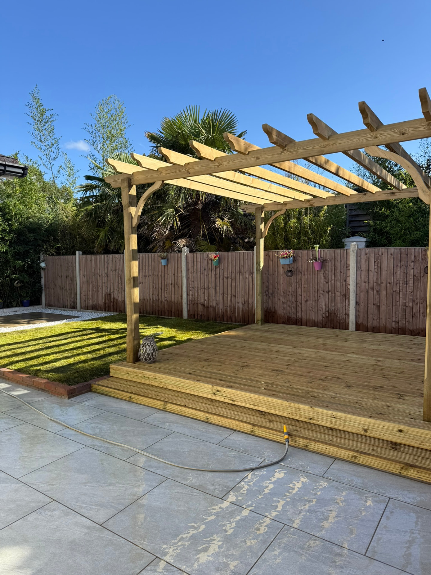 Timber pergola standing over a tiered wooden deck beside a grey tiled patio and lawn