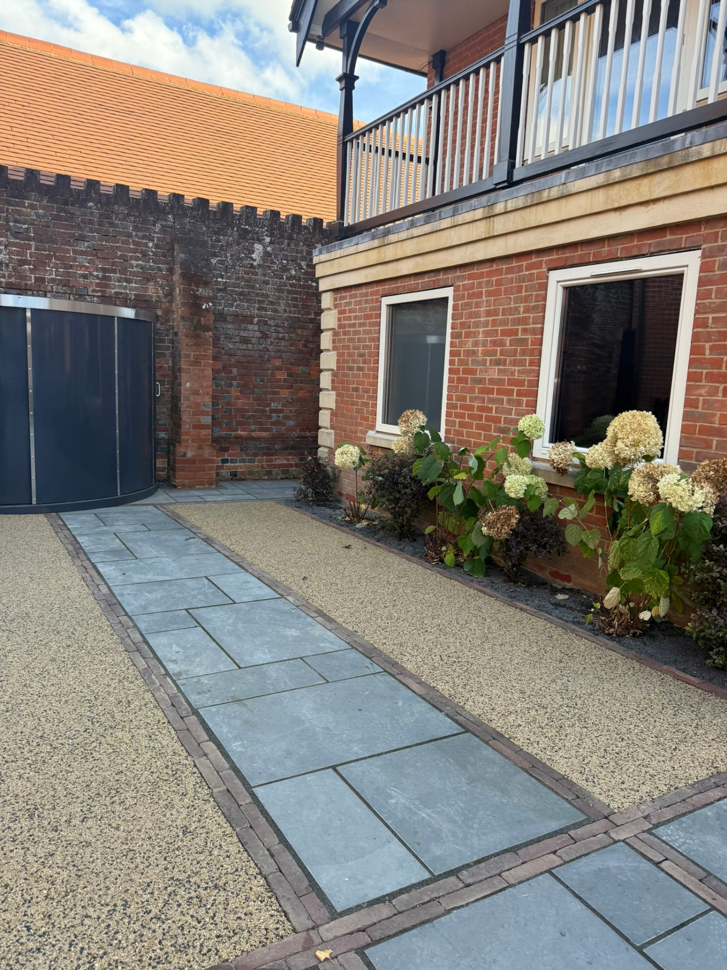Blue-grey natural stone paving slabs laid in a grid with brick borders alongside a resin-bound gravel path beside a red brick house