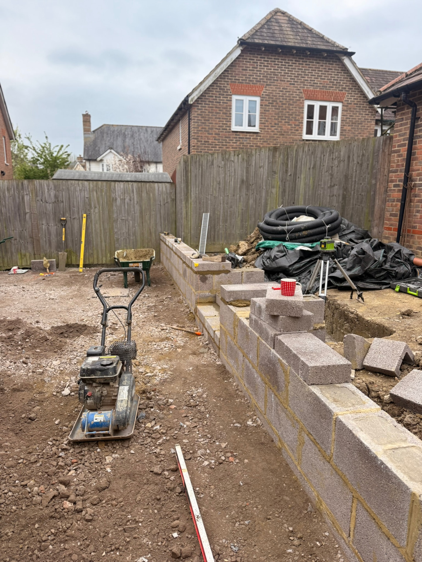 Retaining wall built from grey concrete blocks during construction, with ground being compacted in front of it