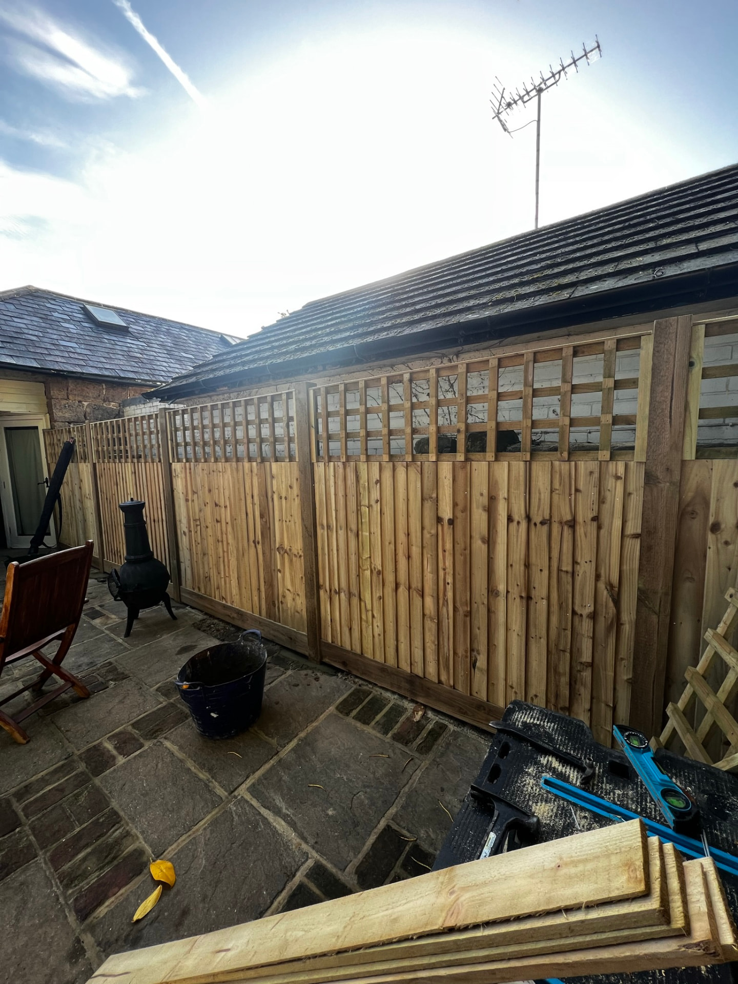 New closeboard wooden boundary fence with a square-grid trellis topper beside a patio of varied stone paving